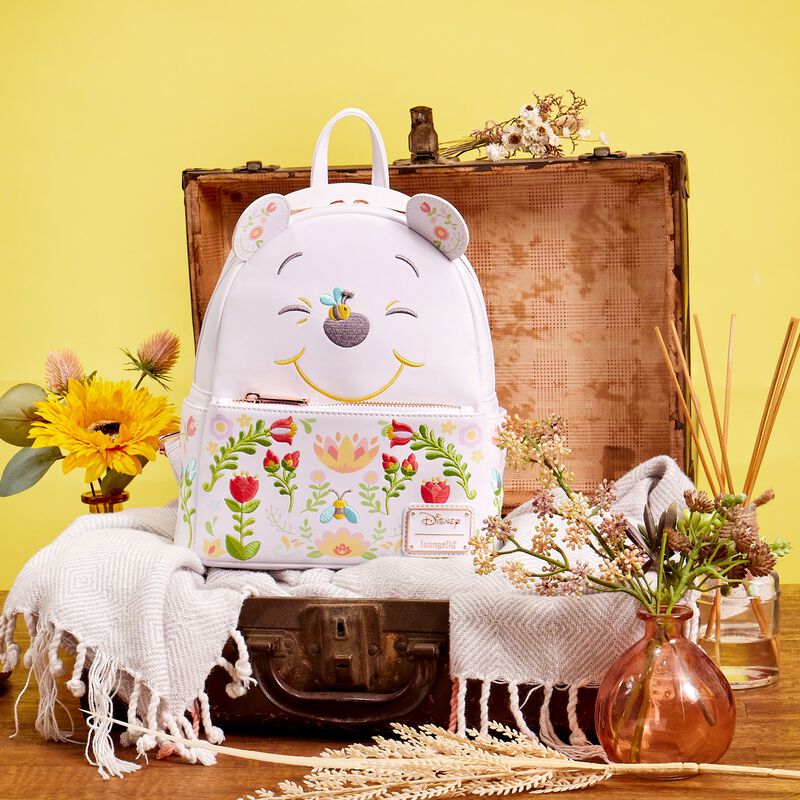 image of the white Winnie the Pooh mini backpack with floral details sitting in an old suitcase surrounded by flowers and a yellow background